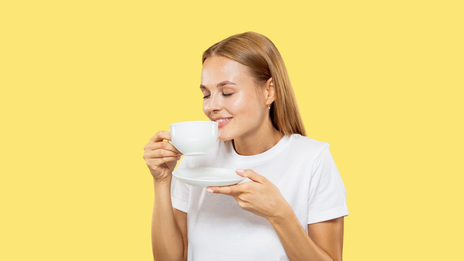 Une jeune femme blonde savoure l'arôme d'une boisson chaude dans une tasse blanche.