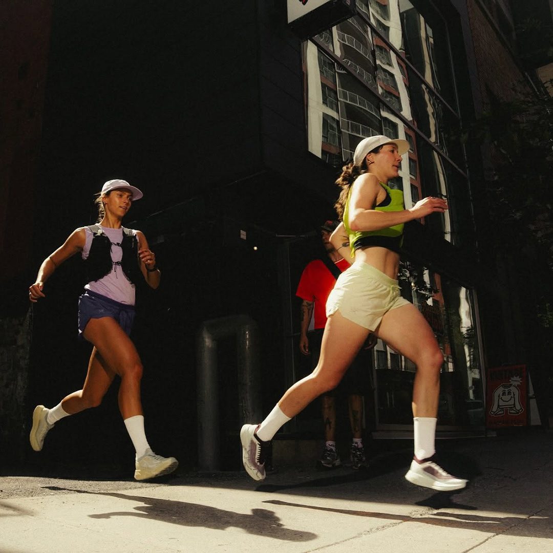 Deux coureuses en tenue sportive courent dans une rue urbaine ensoleillée.