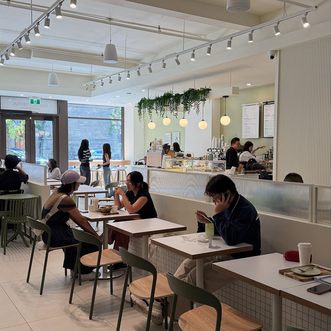 Intérieur lumineux d’un café moderne avec plusieurs clients assis et un comptoir au fond.