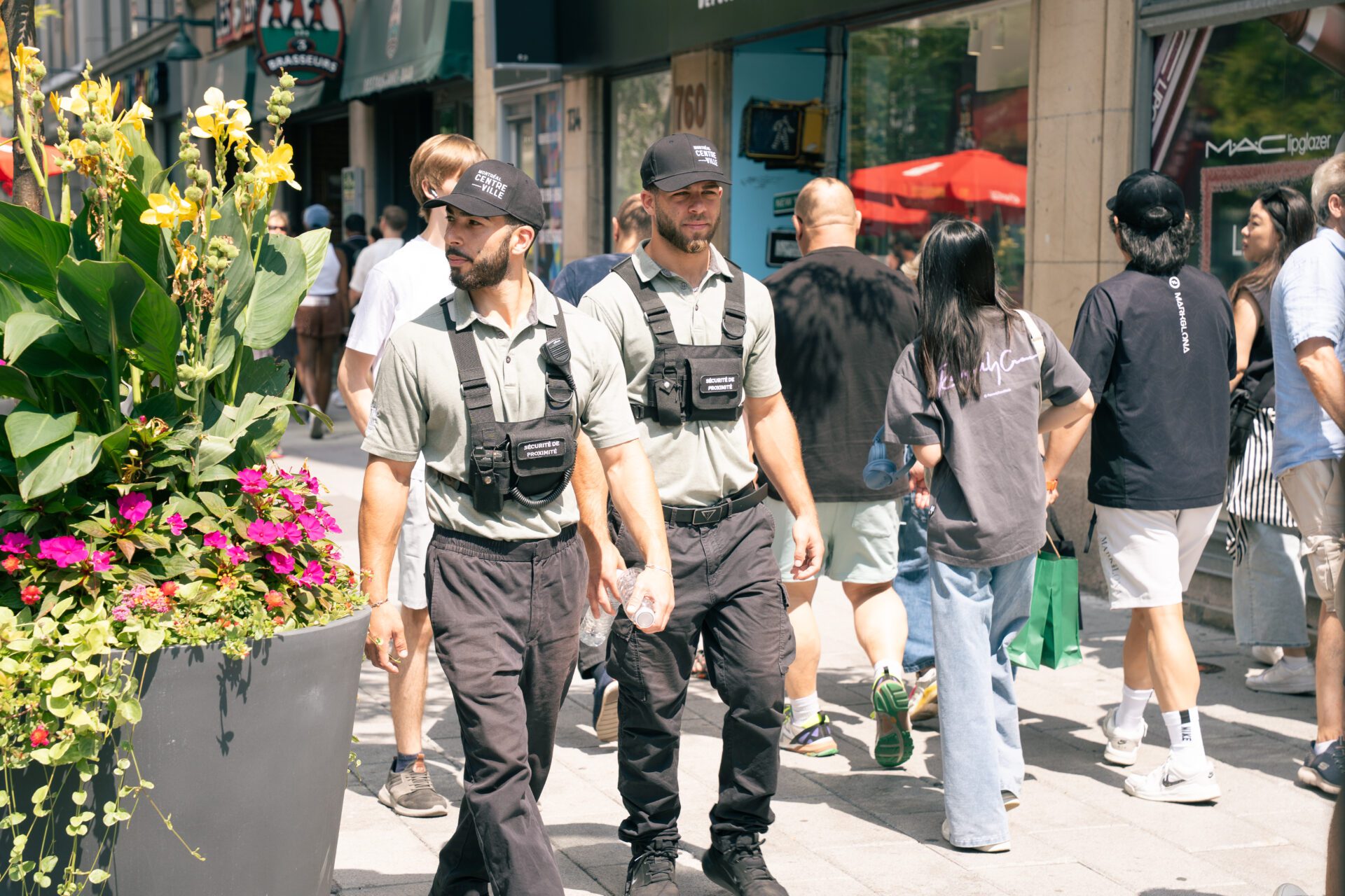 Deux membres de la brigade de sécurité de proximité de Montréal centre-ville marchent sur le trottoir, entourés de passants.