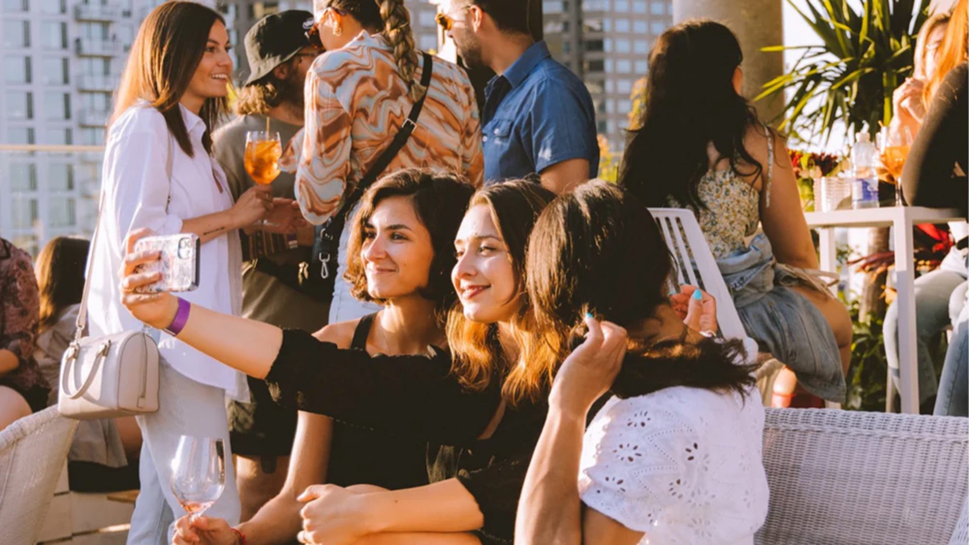 Personnes réunies sur la terrasse de l’Hôtel Monville au coucher du soleil, cocktails à la main avec vue sur le centre-ville de Montréal.