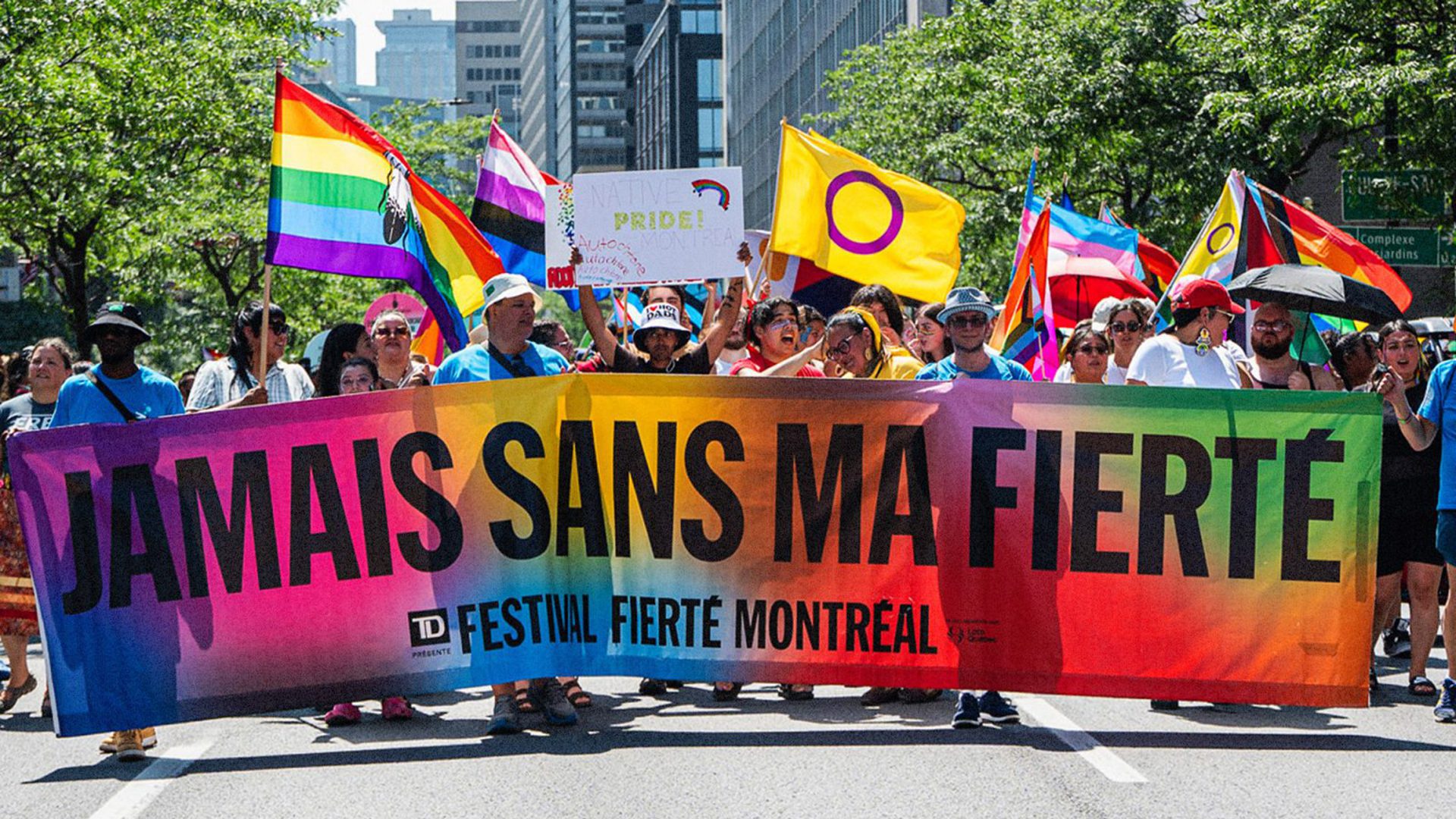 Défilé de la Fierté Montréal avec des participants brandissant des drapeaux arc-en-ciel dans le centre-ville.